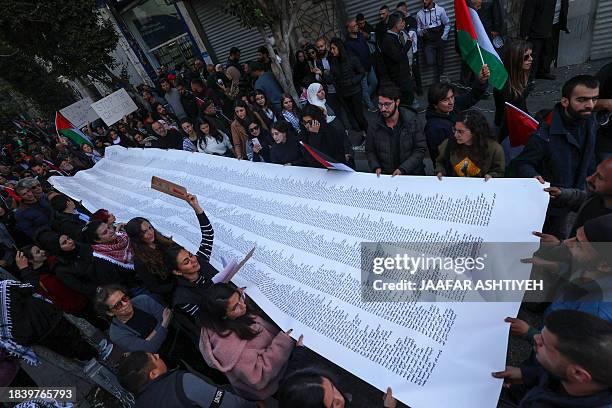 Palestinians carry a list of Gaza victims during a rally amid a general strike in Ramallah city in the occupied West Bank on December 11 in...