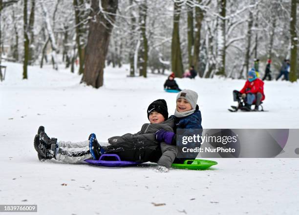 Two boys are holding on tight to each other as they ride plastic saucer sledges in Lviv, Ukraine, on December 10, 2023.