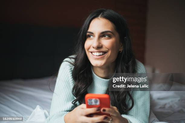 smiling woman relaxing in bed using her mobile phone - beautiful women bed stockfoto's en -beelden