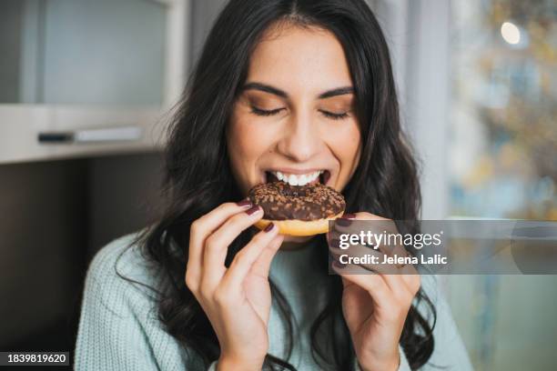 porträt einer jungen frau, die in der küche einen donut isst - zucker stock-fotos und bilder