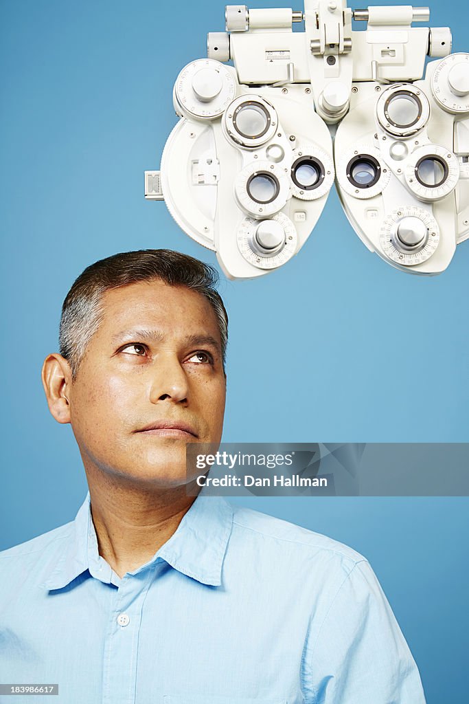 Man stares at phoropter on blue background