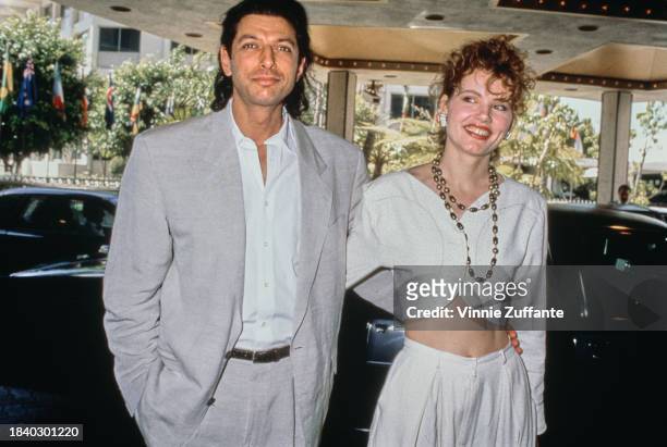 American actor Jeff Goldblum, wearing a grey suit over a white shirt, and his wife, American actress Geena Davis, who wears a white outfit with her...