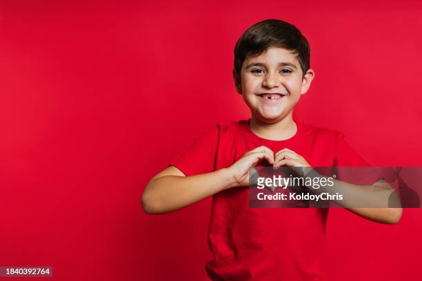 happy caucasian boy making heart shape with hands on red background - heart stock pictures, royalty-free photos & images