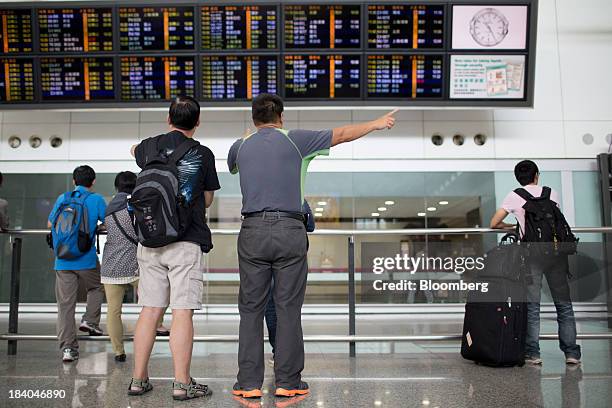 People stand in front of electronic panels displaying flight information in the arrival hall at Hong Kong International Airport in Hong Kong, China,...