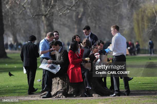 Workers share a tree stump as they eat lunch enjoying the warm weather in a park in central London on March 15, 2012. AFP PHOTO / CARL COURT