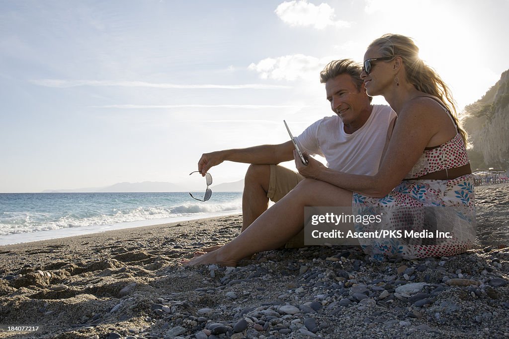 Couple relax on beach, using digital tablet