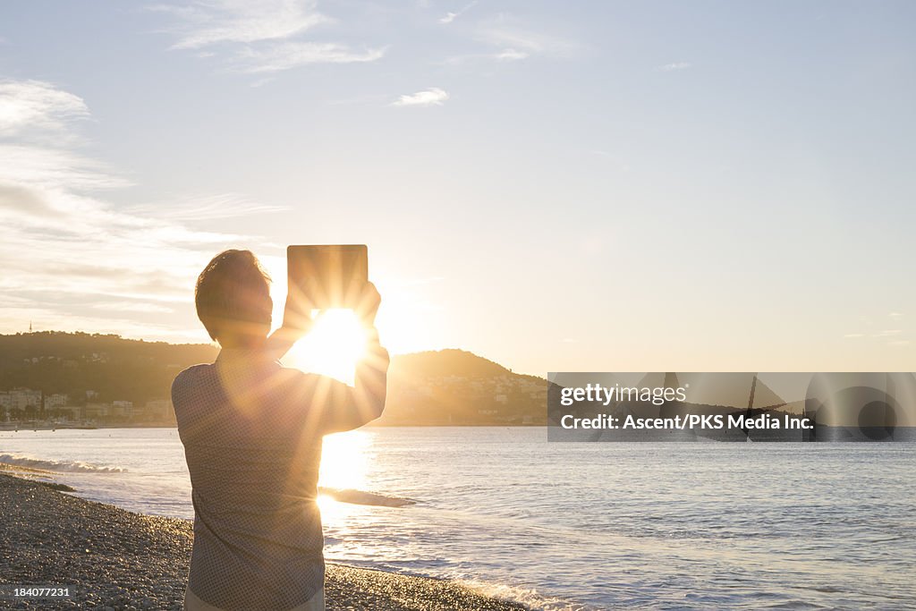 Man takes picture of sunrise over city, tablet