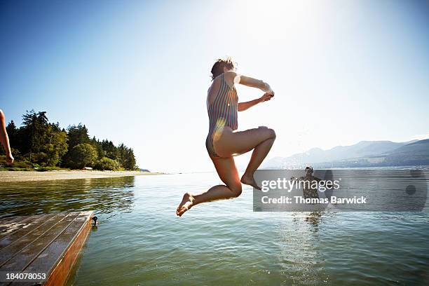 woman jumping off of floating dock into water - jumping into lake stock-fotos und bilder