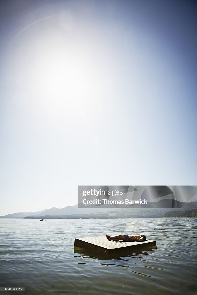 Man lying on floating dock mountains in background
