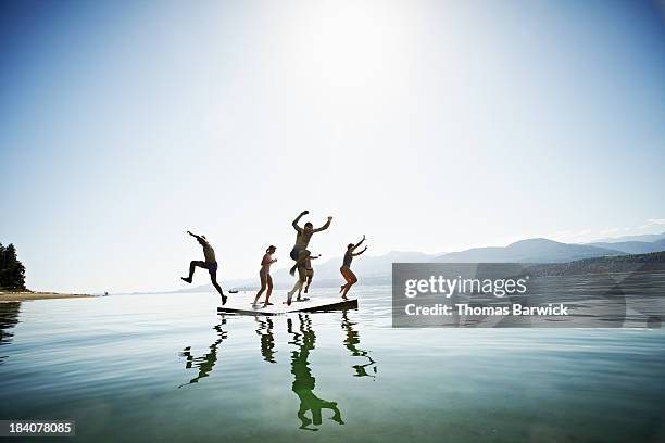 group of friends jumping off floating dock - bundesstaat washington stock-fotos und bilder
