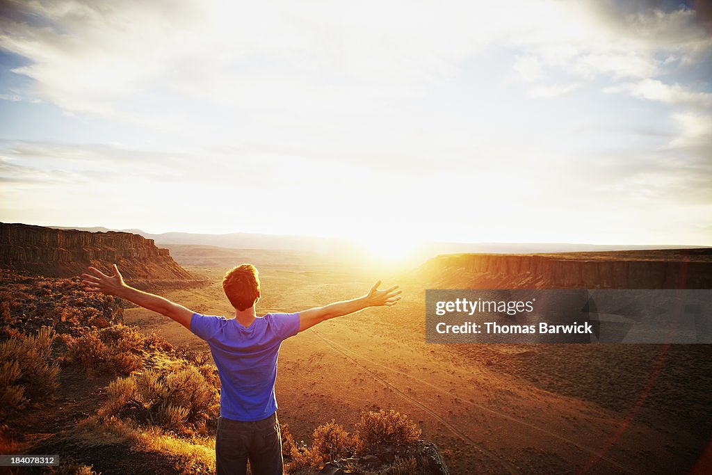 Man standing with arms outstretched at sunset