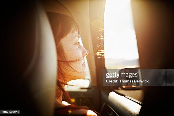 woman with hair blowing looking out window of car - sunny side fotografías e imágenes de stock