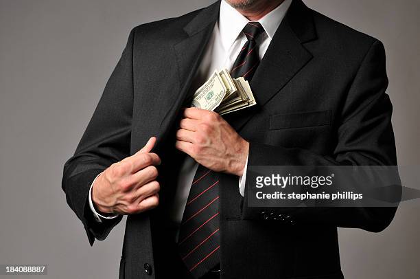 businessman slipping a stack of cash into his suit pocket - bribing stock pictures, royalty-free photos & images