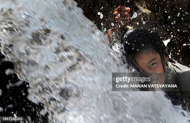 Young Indian girl plays under a broken water pipe in New Delhi on June 7, 2009. The unrelenting heat is persisting in the Indian capital as...