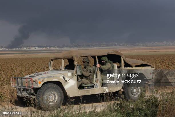 An Israeli military vehicle drives past billowing smoke in the distance at the border with the Gaza Strip on December 12 amid ongoing battles with...