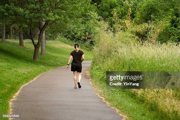 woman walking away on footpath, jogging or hiking in park - asphalt stock pictures, royalty-free photos & images