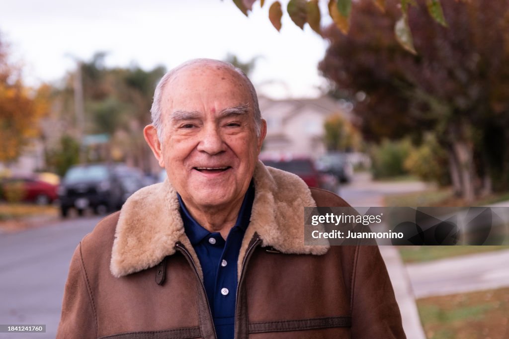 Smiling hispanic senior man looking at the camera posing in his neighborhood street