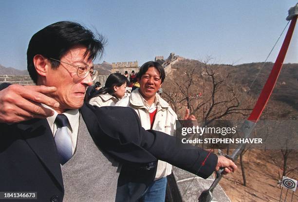 Man grimaces as he releases an arrow from the Great Wall at targets below, as warriors did thousands of years ago, as throngs of Chinese and Western...