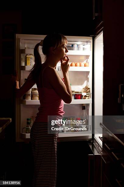 young woman craving food choosing near refrigerator at night - craving food stock pictures, royalty-free photos & images
