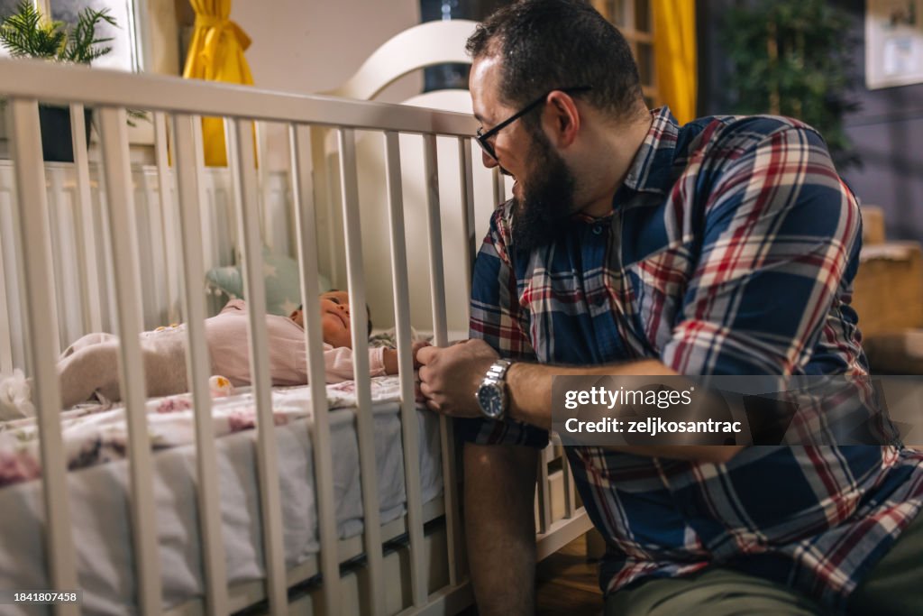 A young father lulls his baby to sleep while playing the guitar and singing