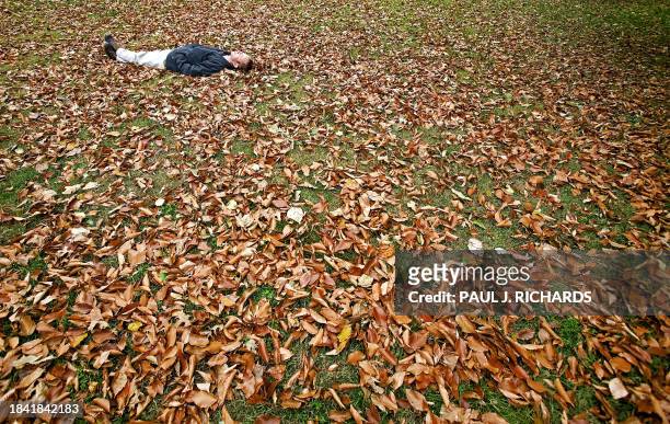 An unidentified man relaxes on grass of Lafayette Park covered with Fall leaves across the street from the White House 14 November 2006 in...