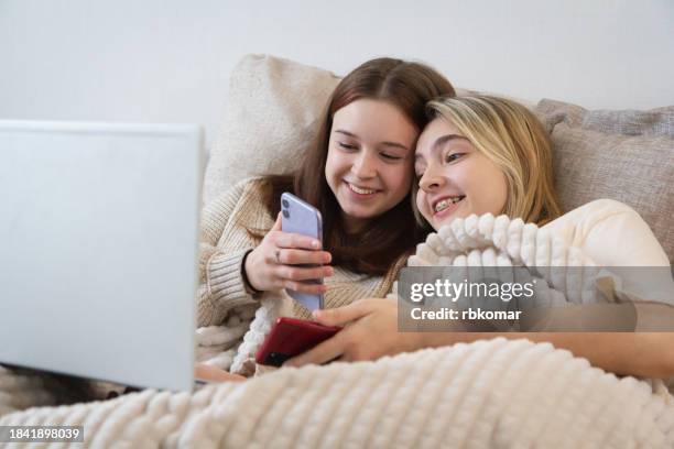 social media - teenage girls looking at smartphones while lying on bed - student girl using laptop computer and smart phone stock-fotos und bilder