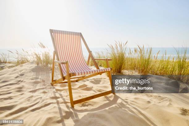 striped deck chair at sand dunes with marram grass against sea and sunlight - sedia da giardino foto e immagini stock