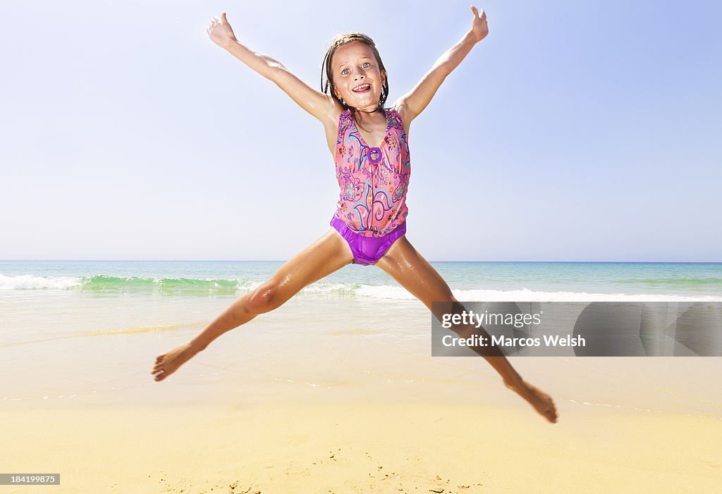 Young girl jumping at beach with arms in the air