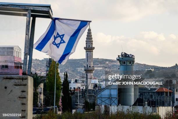 An Israeli flag flies at a checkpoint in front of an Israeli army watchtower next to a minaret at the al-Aroub camp for Palestinian refugees south of...