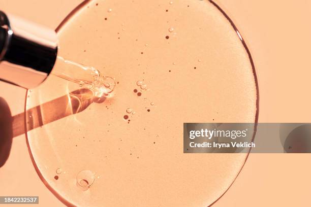 glass pipette with face serum or essential oil with oxygen aqua bubbles and a drop of liquid on a pastel beige orange background with shadow in peach color. - antioxidant serum stock pictures, royalty-free photos & images