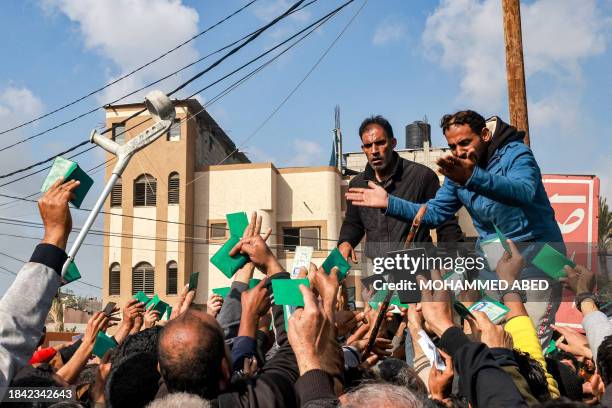 Palestinians wave their identity cards as they gather to receive flour rations for their families outside a warehouse of the United Nations Relief...