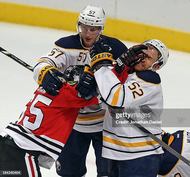 Andrew Shaw of the Chicago Blackhawks shoves Alexander Sulzer of the Buffalo Sabres in the face as Tyler Meyers tries to break it up at the United...