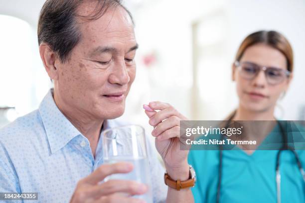 set up a medication reminder and tracking system for taking medication management for seniors safely. a senior male patient holding a drinking glass and medicine pill while a home nurse beside him gave advice. - antibiótico fotografías e imágenes de stock