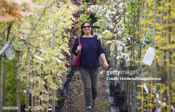 Model released woman walking past rows of colourful trees in blossom at a garden centre.