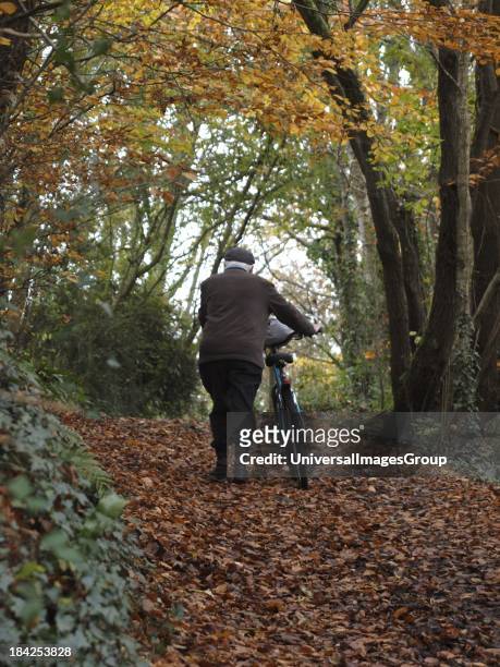 Old man pushing bicycle up a hill, Autumn, UK.