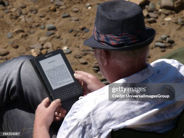 Man reading Kindle e-book reader at the beach, UK.