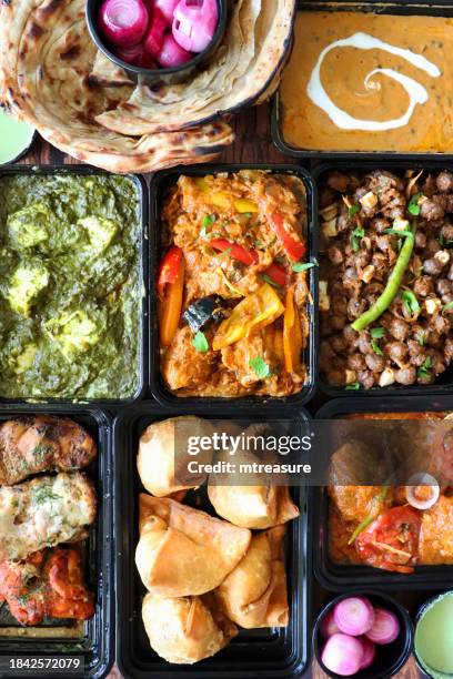 image of indian takeaway dishes in black plastic, single-use food containers, kadai chicken, chicken bhuna, palak paneer, samosas,  murgh malai tikka, pink pickled onions, mint and coriander dip, lachha paratha, pindi chole and dal makhani, elevated view - paneer tikka stock pictures, royalty-free photos & images