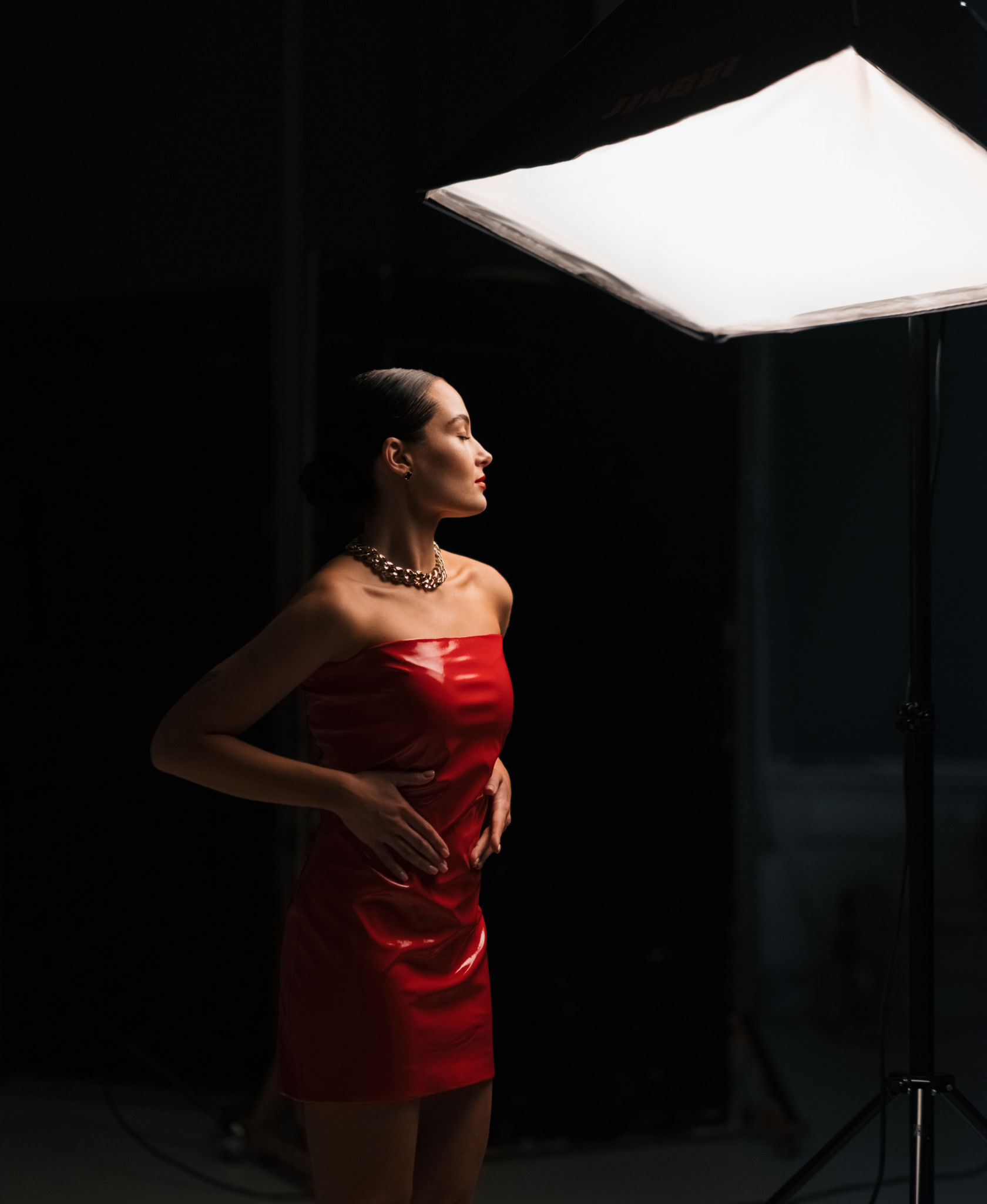 Young pretty woman poses in red latex dress under spotlight in studio. Young pretty woman poses in red latex dress under spotlight in studio.