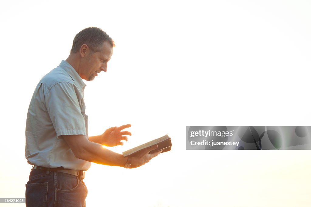 Pastor casually dressed walking in sunlight reading Bible