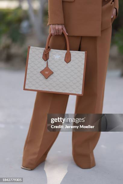 Katya Tolstova seen wearing Aknvas brown suit blazer jacket, matching Aknvas brown suit wide leg pants, MCM brown / cream white shopper bag and...