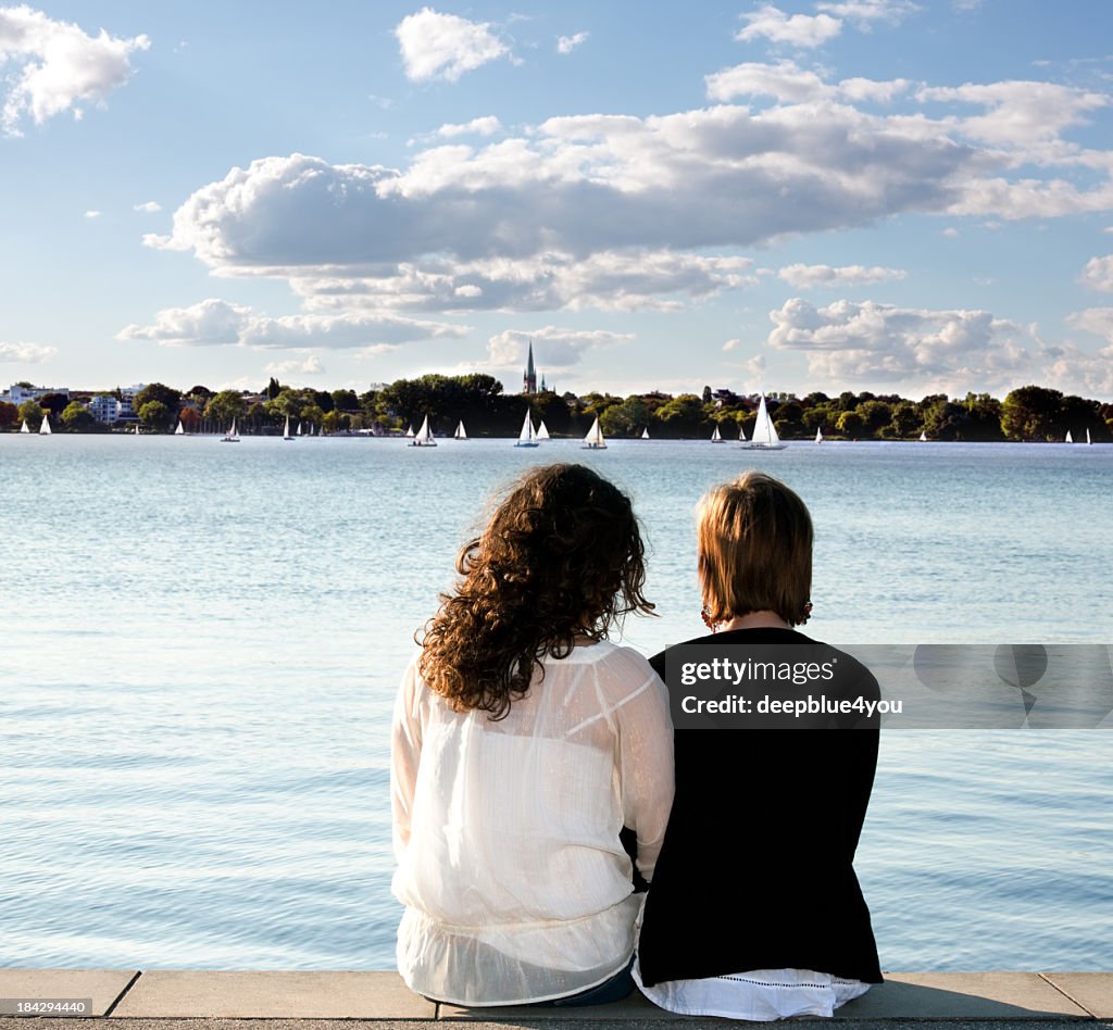 Girlfriends sitting on pier looking out over water