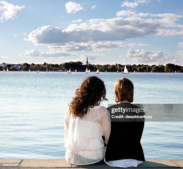 girlfriends sitting on pier looking out over water - alster river stock pictures, royalty-free photos & images