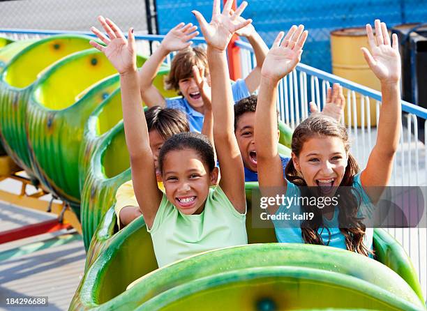 children riding a green roller coaster - theme park ride stock pictures, royalty-free photos & images