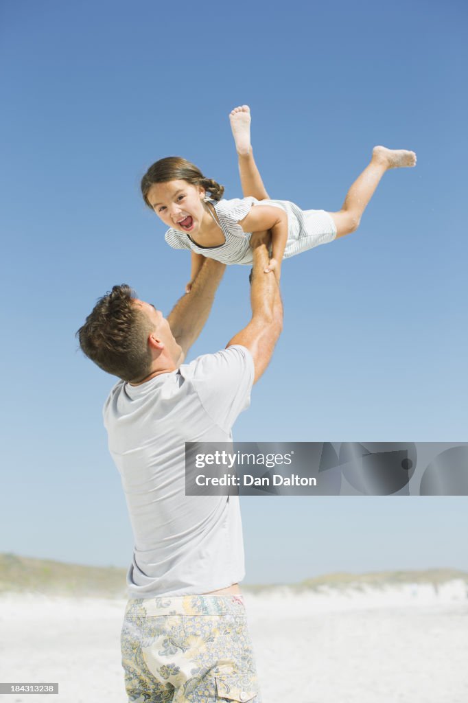Father lifting daughter overhead on beach