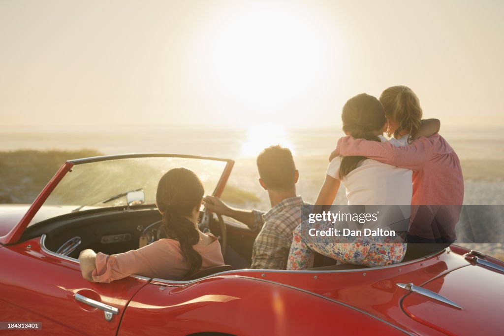 Family watching sunset over ocean from convertible on beach