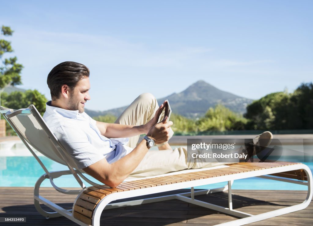 Man using digital tablet on lounge chair at poolside