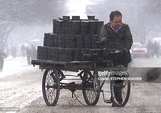 Man braces against freezing winds and snow as he pushes his tri-cycle loaded with compressed coal across a downtown street Beijing 11 January 2000....