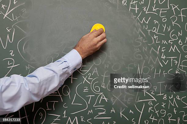 human hand erasing blackboard with large amount of letters - board eraser stock pictures, royalty-free photos & images