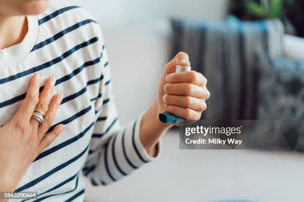 woman using an asthma inhaler indoors. using medication during an asthma attack. - asthmainhalator stock-fotos und bilder