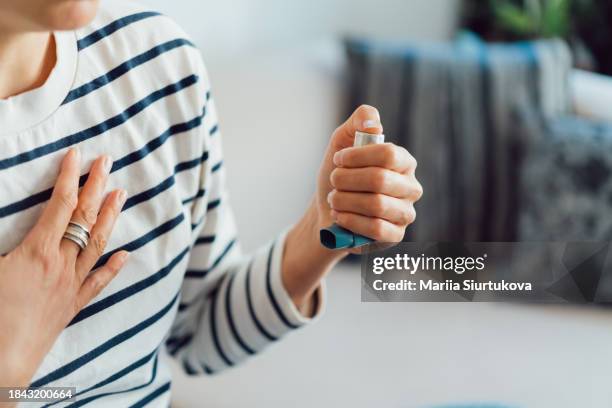 woman using an asthma inhaler indoors. using medication during an asthma attack. - asthmatique photos et images de collection